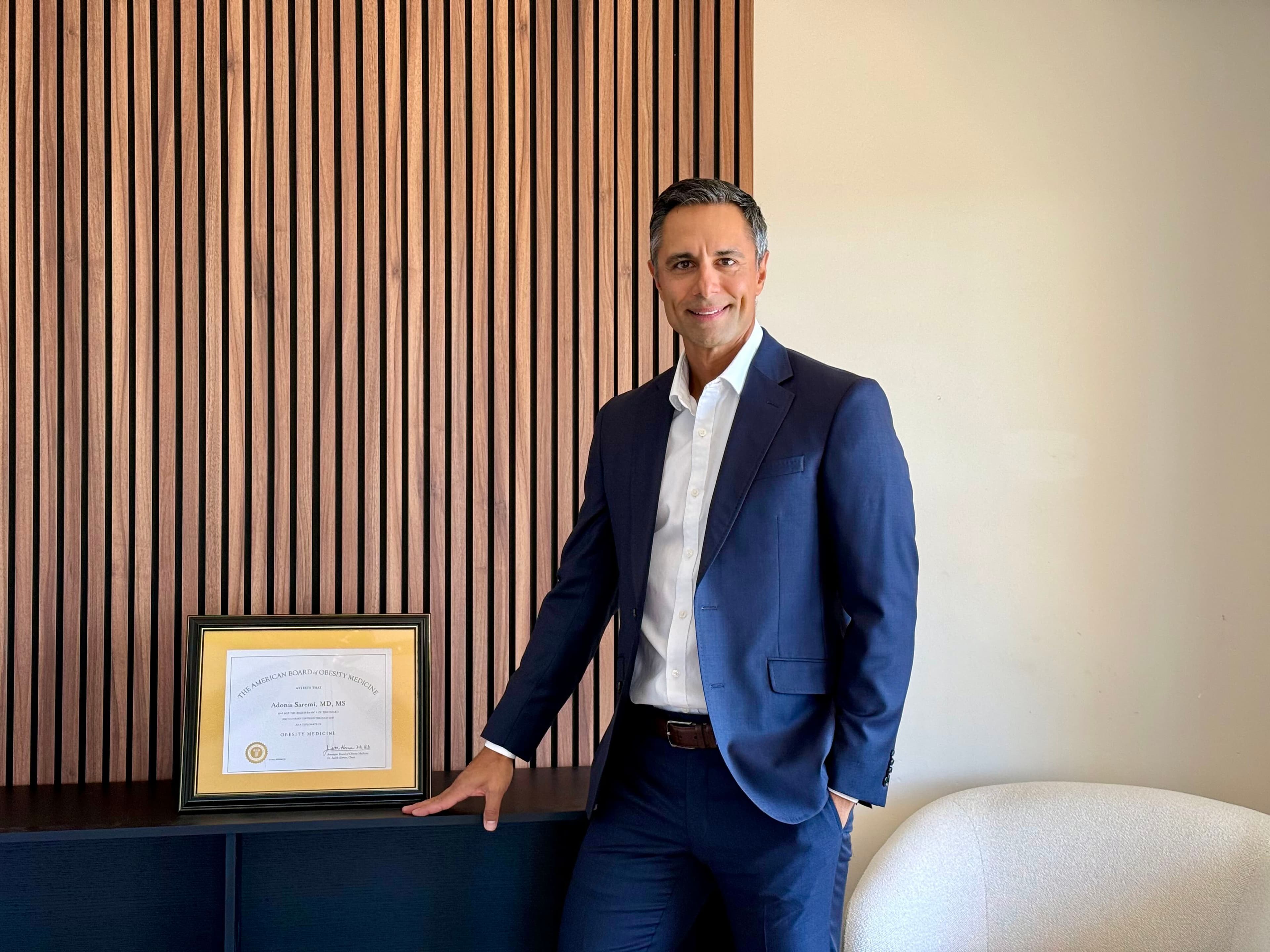 Dr. Adonis Saremi in his office, beside his American Board of Obesity Medicine diplomate certificate